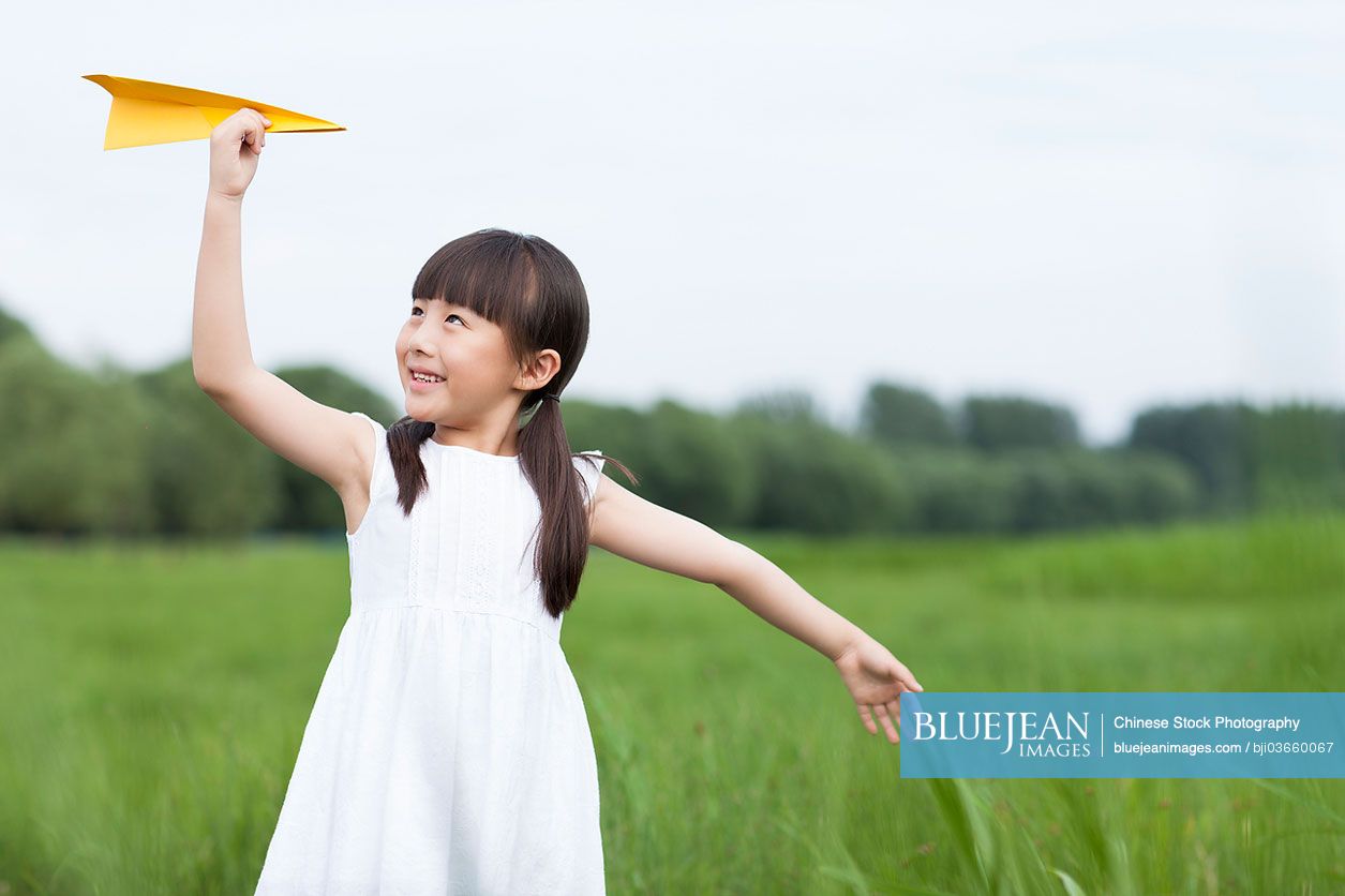 Happy Chinese girl playing paper airplane in the open air