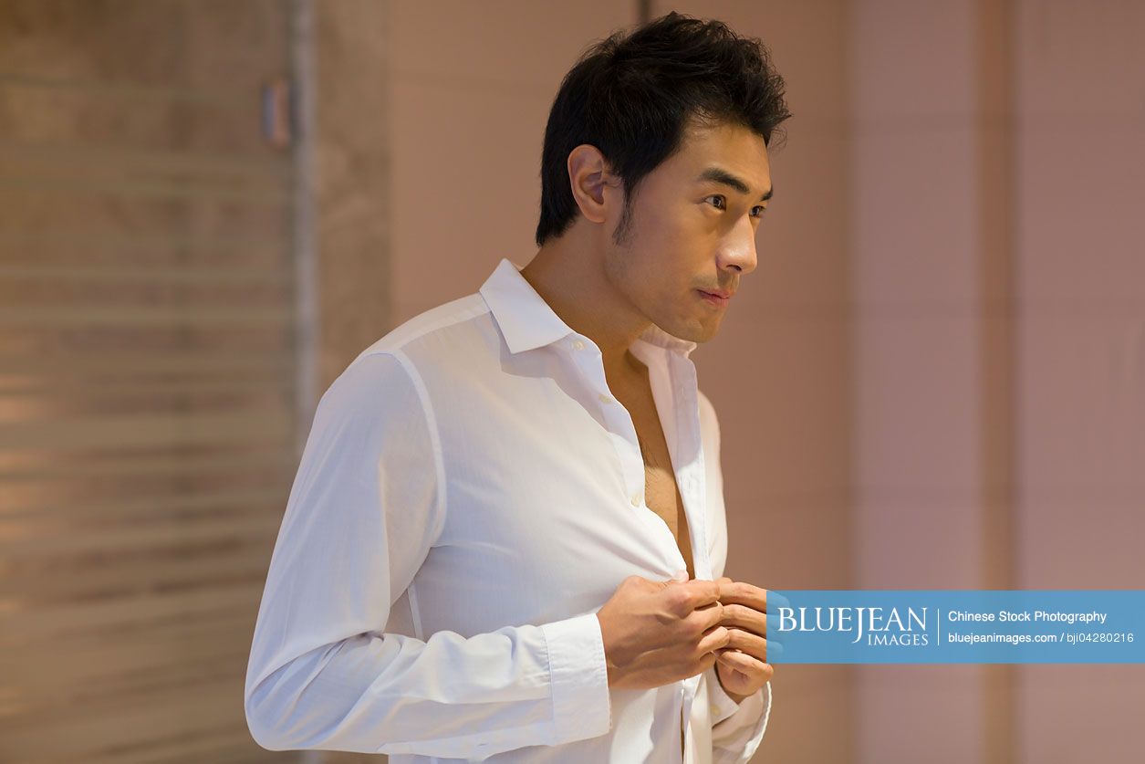 Young Chinese man buttoning shirt