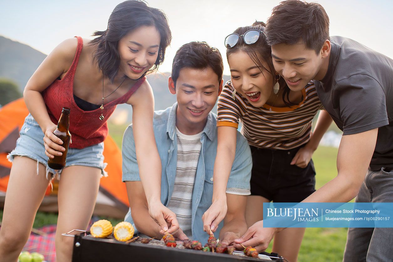 Happy young Chinese friends barbecuing outdoors