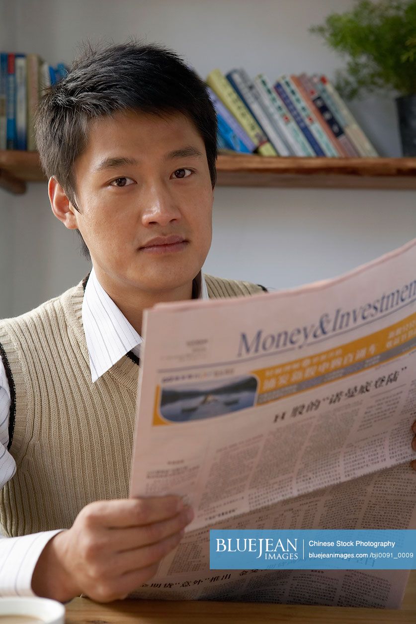 Chinese Man Sitting At Table, Reading A Newspaper
