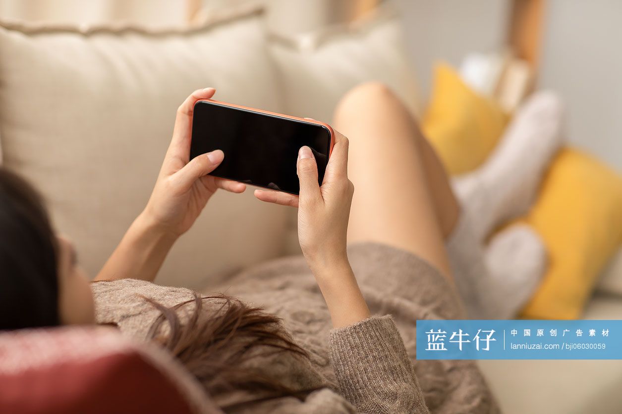 年轻女士躺在沙发上玩手机游戏