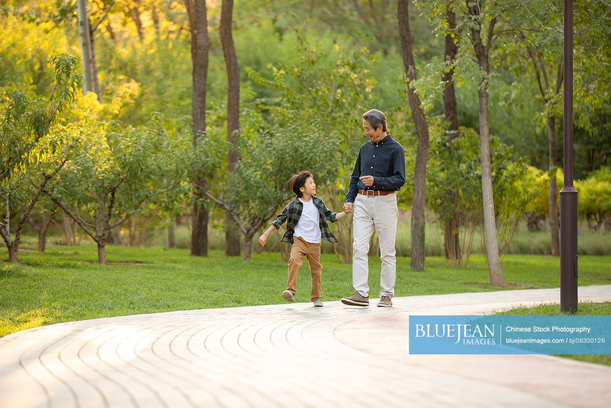 Happy Chinese grandfather and grandson walking in park