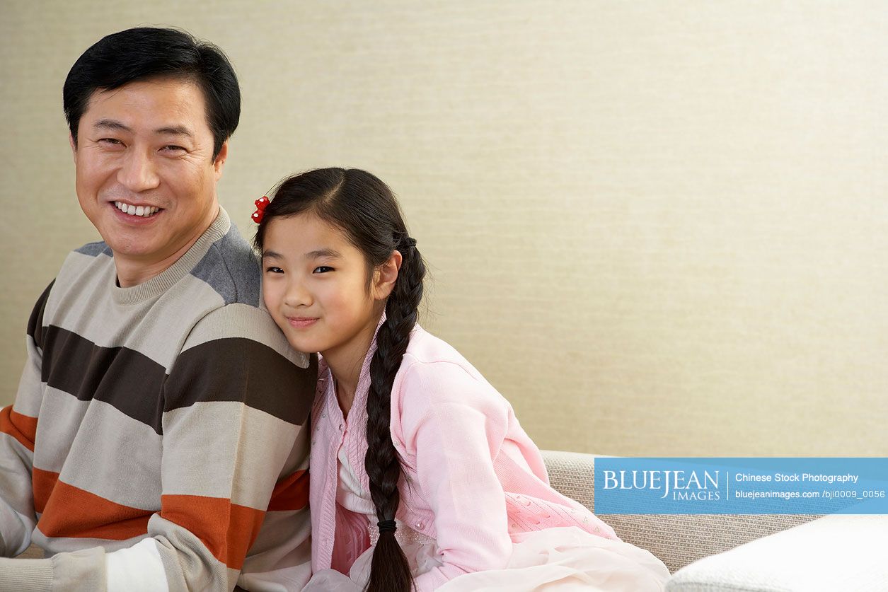 Chinese Father And Daughter Sitting On The Couch Together