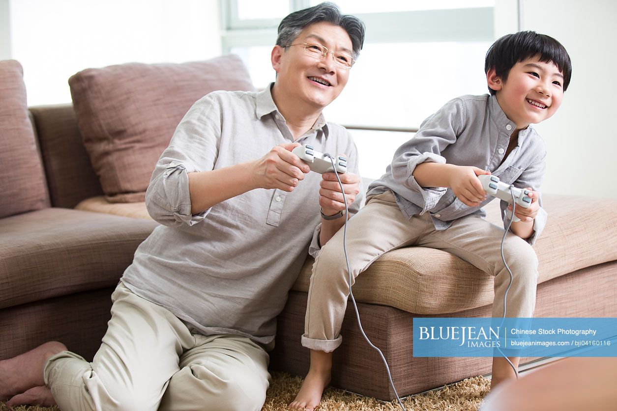 Cheerful Chinese grandfather and grandson playing video game