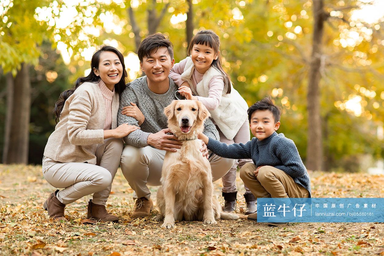 快乐的年轻家庭和狗在秋日的树林里