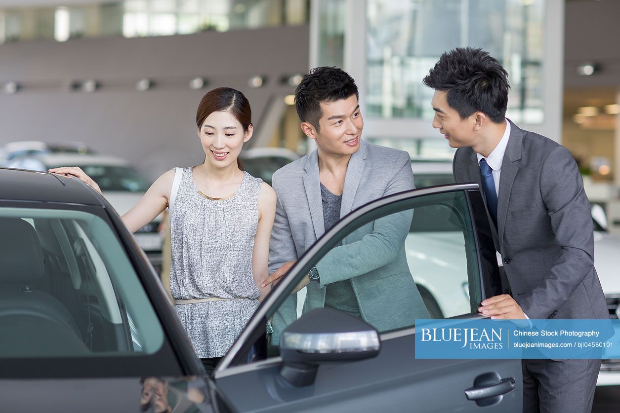 Young Chinese couple choosing car in showroom
