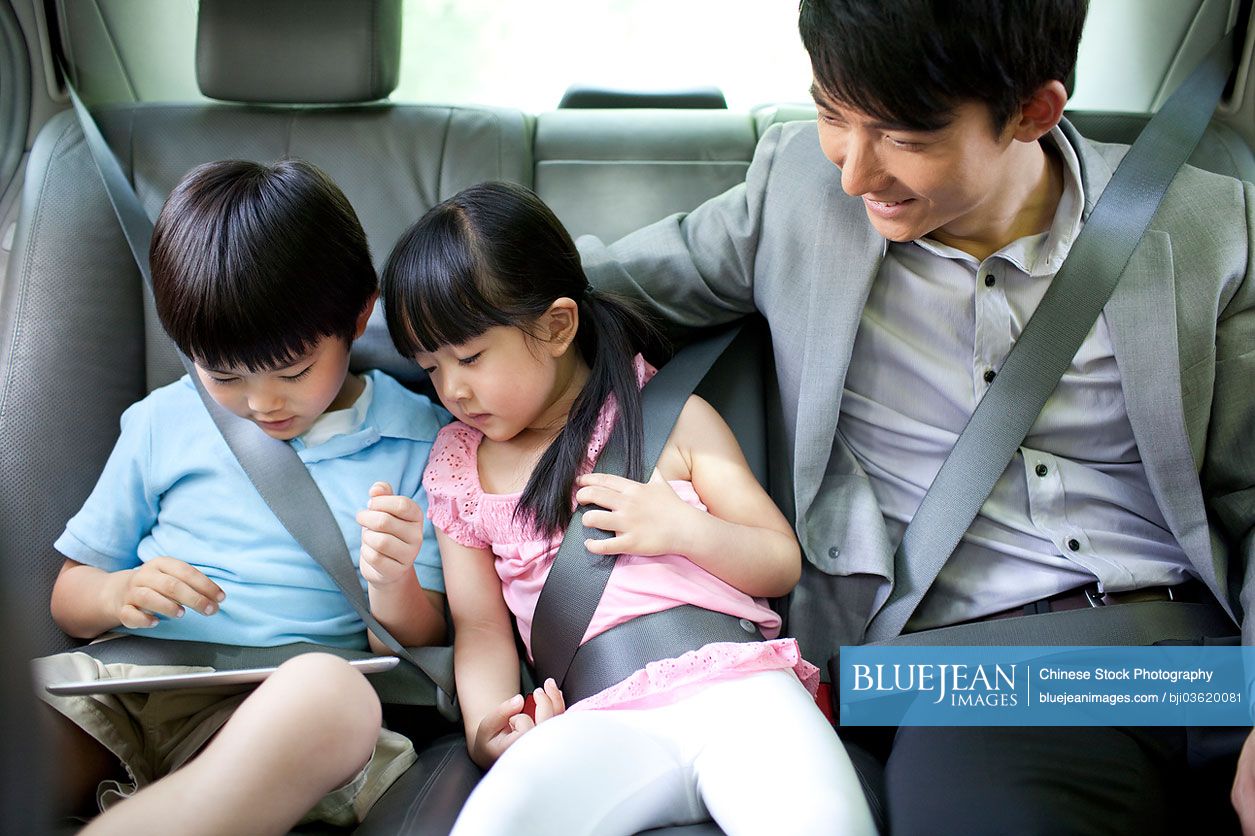 Happy Chinese family playing digital tablet in car
