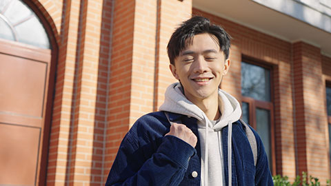 Happy Chinese college boy standing in front of teaching building