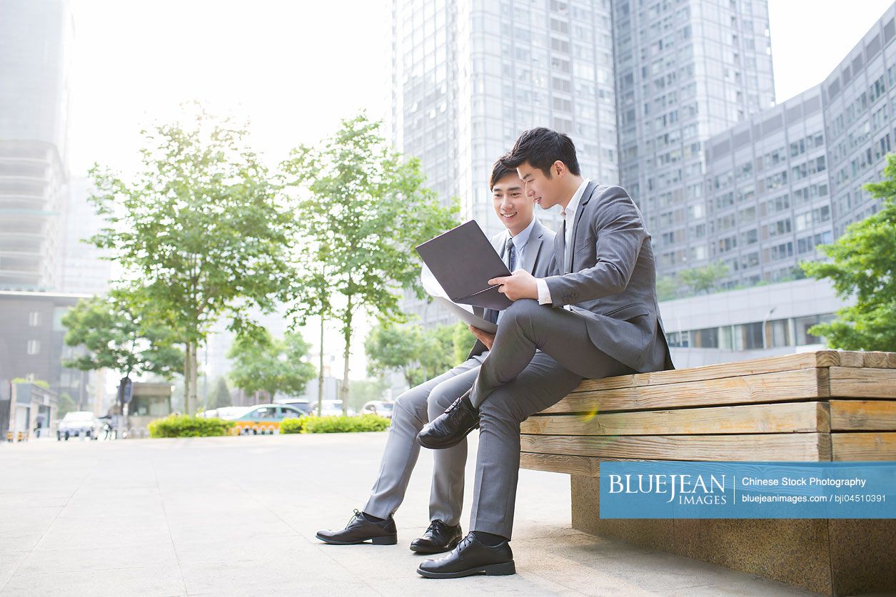 Young Chinese business person working with laptop outdoors