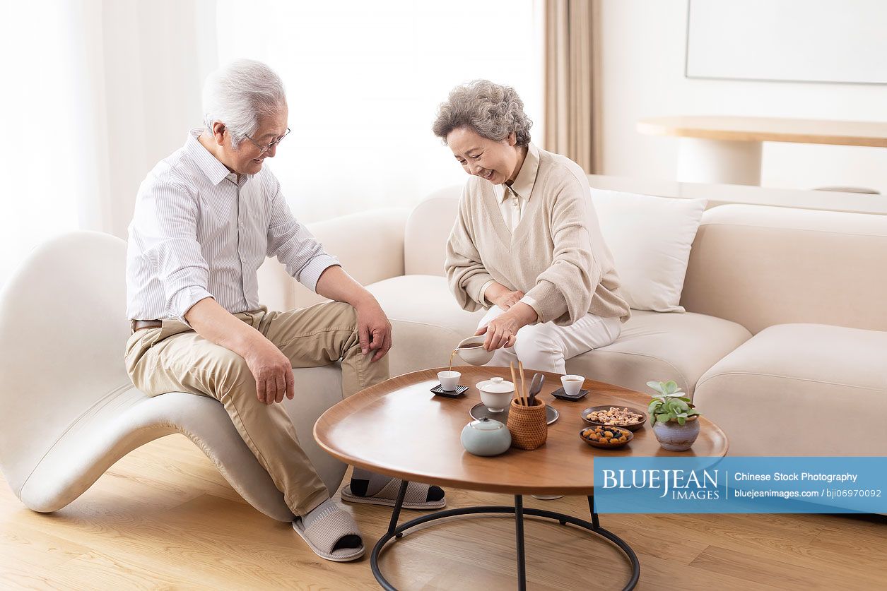 Cheerful senior Chinese couple drinking tea at home