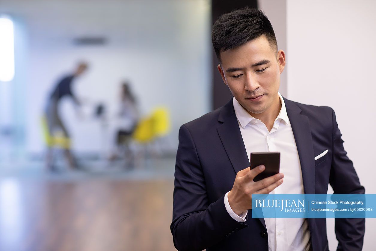 Confident young Chinese businessman using smart phone