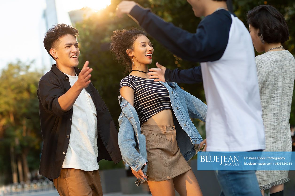 Fashionable young friends greeting and hugging on street