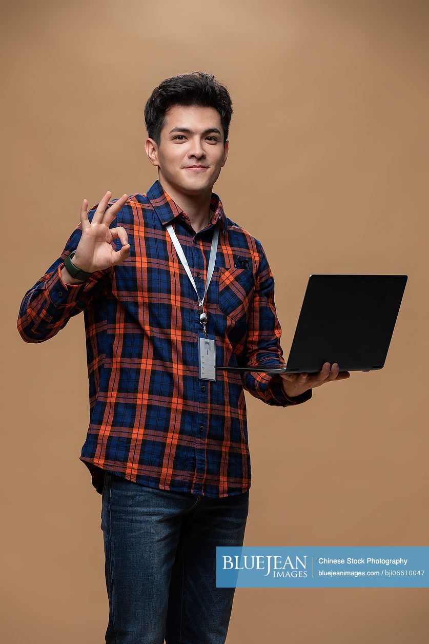 Cheerful young Chinese man holding a laptop