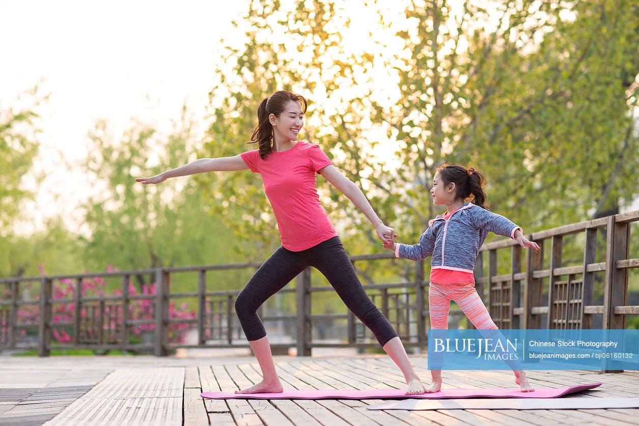 Happy Chinese mother and daughter doing yoga outdoors