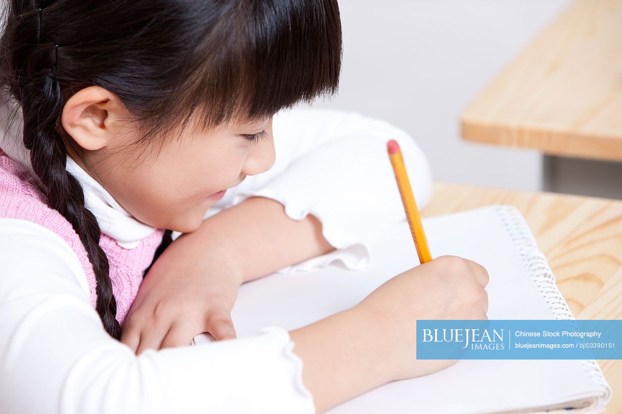 Lovely Chinese schoolgirl writing in classroom