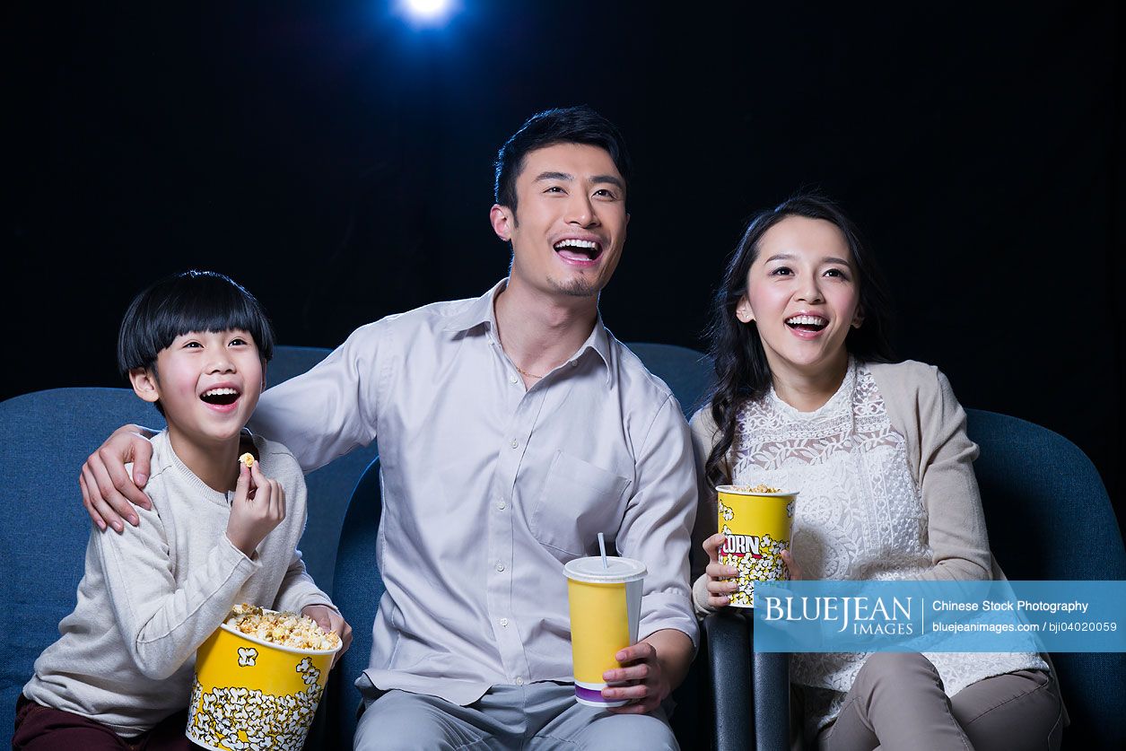 Young Chinese family watching movie in cinema