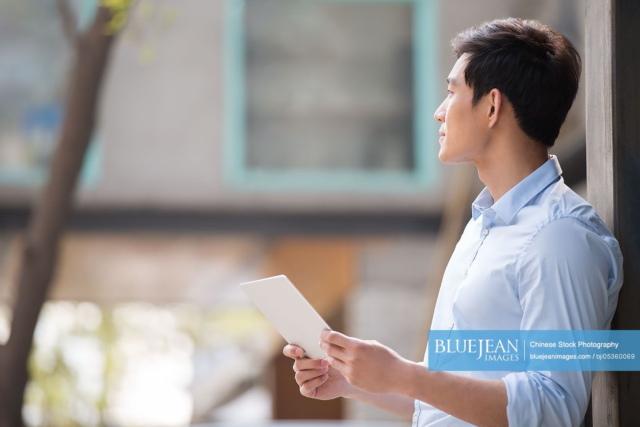 Young Chinese businessman holding a digital tablet outdoors