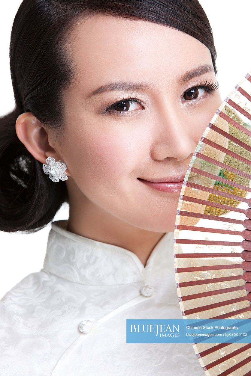 Beautiful young Chinese woman in traditional cheongsam with folding fan