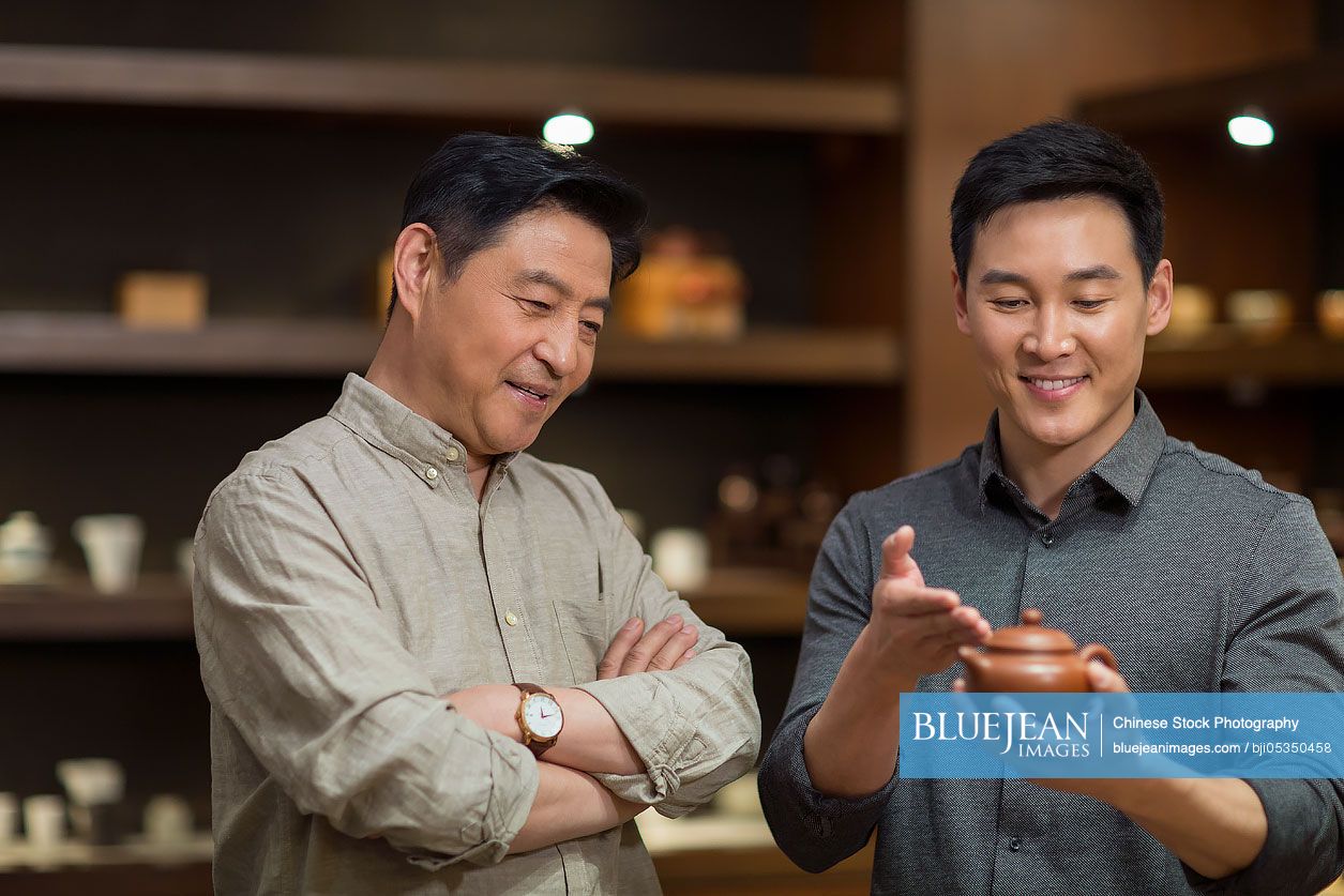 Mid adult Chinese man showing a teapot to customer