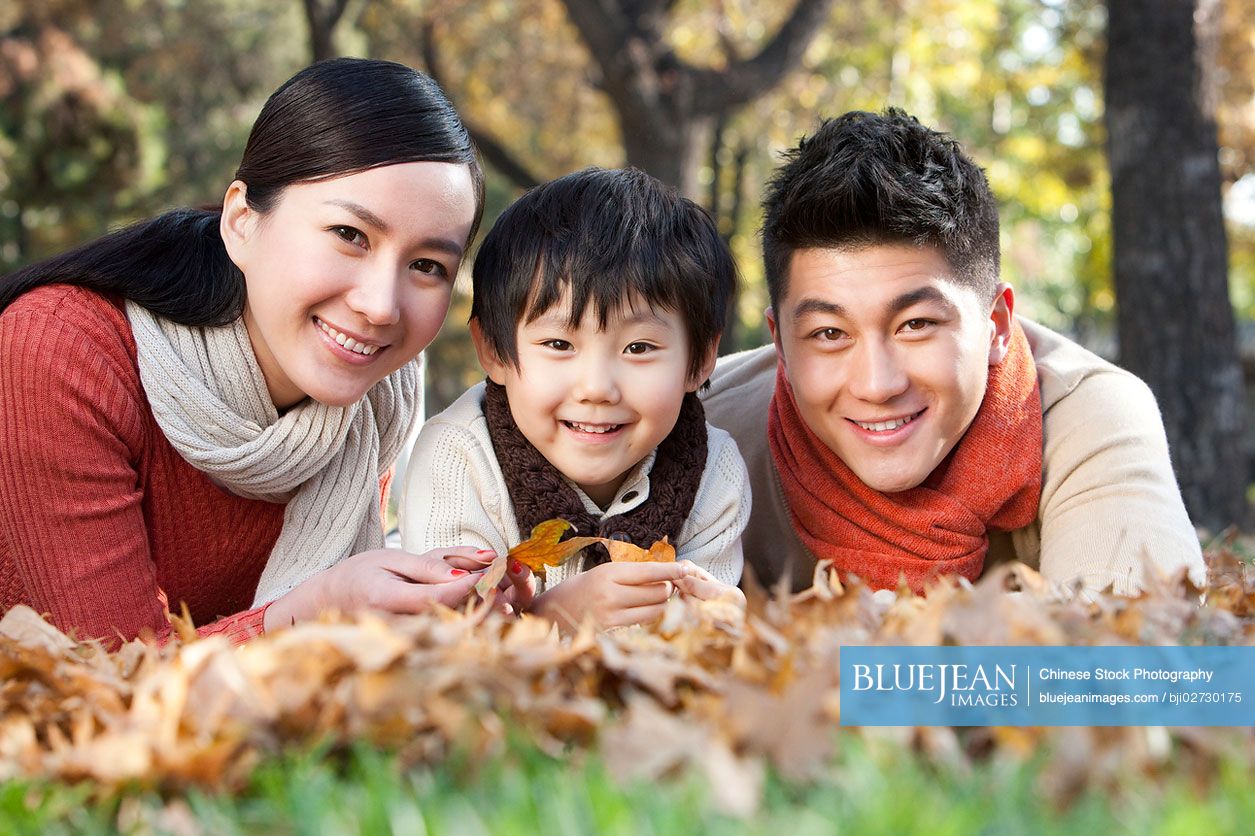 Young Chinese family lying on the grass surrounded by autumn leaves