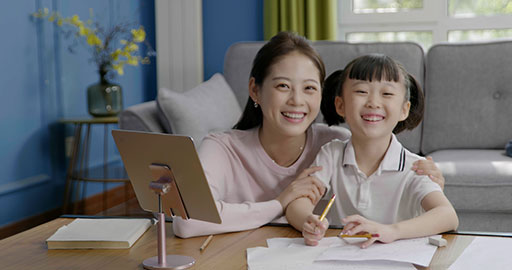 Little girl taking an online class with her mom keeping her company