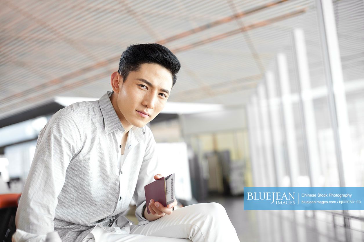 Young Chinese man waiting in airport lounge with flight ticket and passport