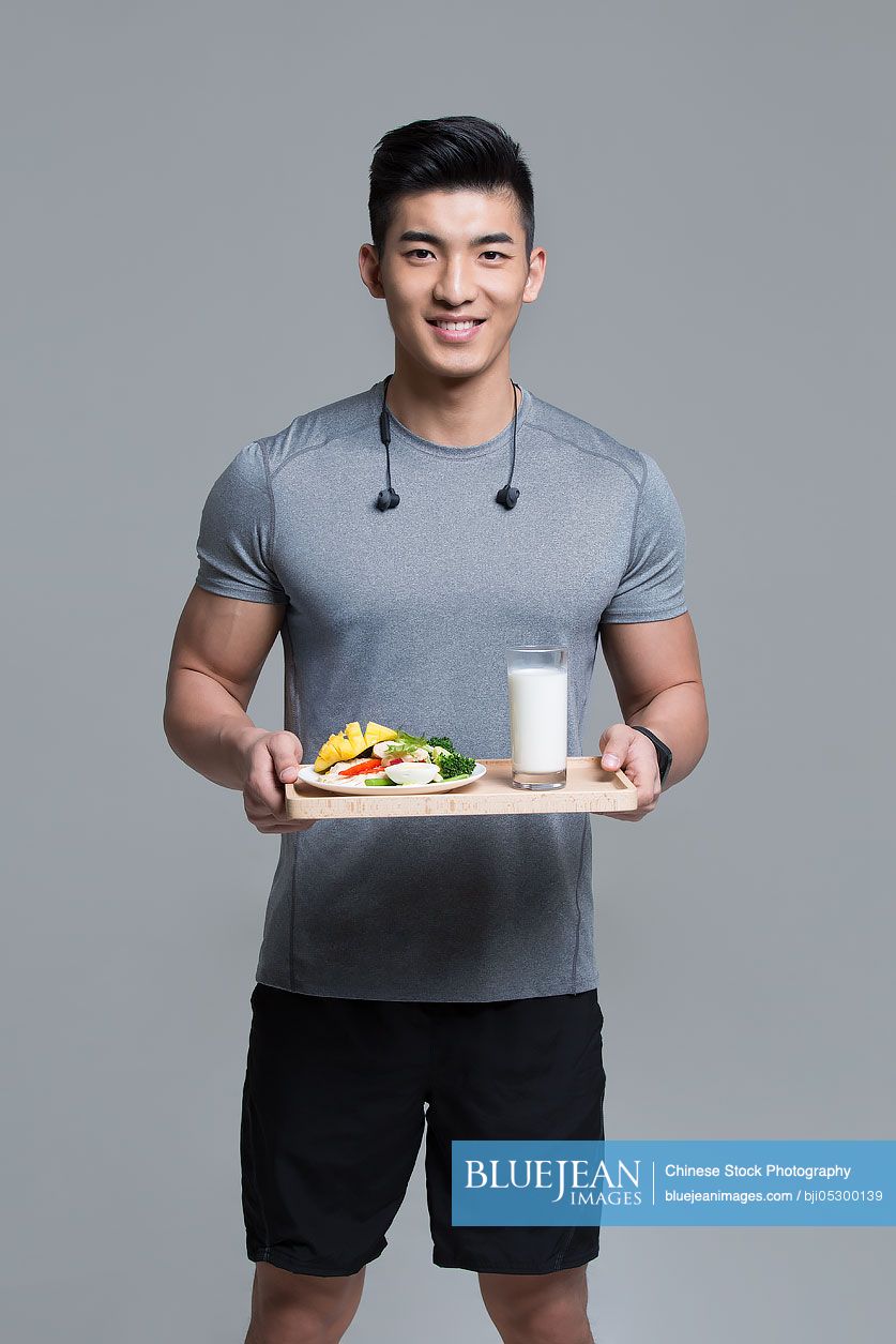 Young Chinese male athlete holding vegetable salad and milk while exercising