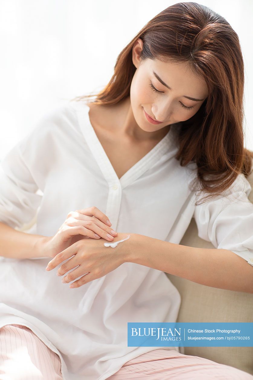 Young Chinese woman applying moisturizer at home
