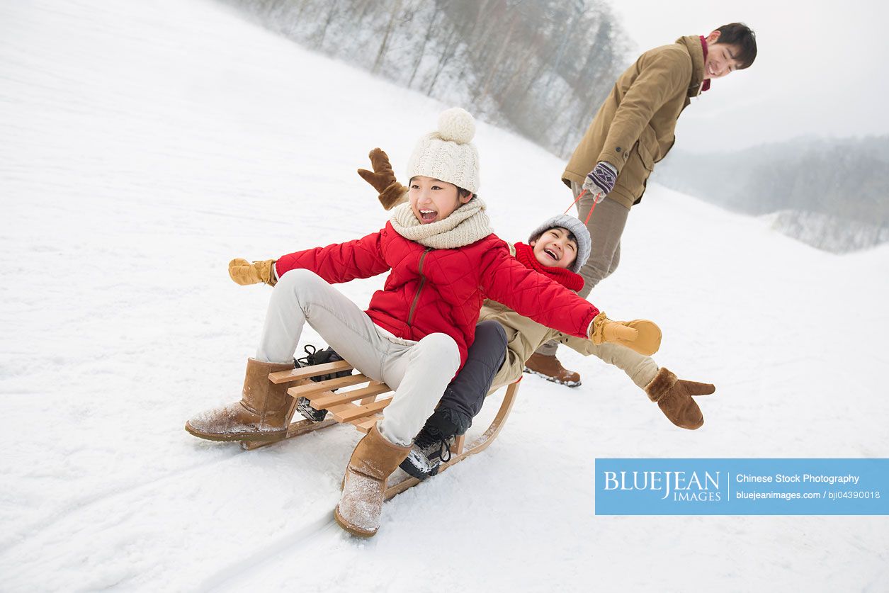 Young Chinese father pulling his children on sled