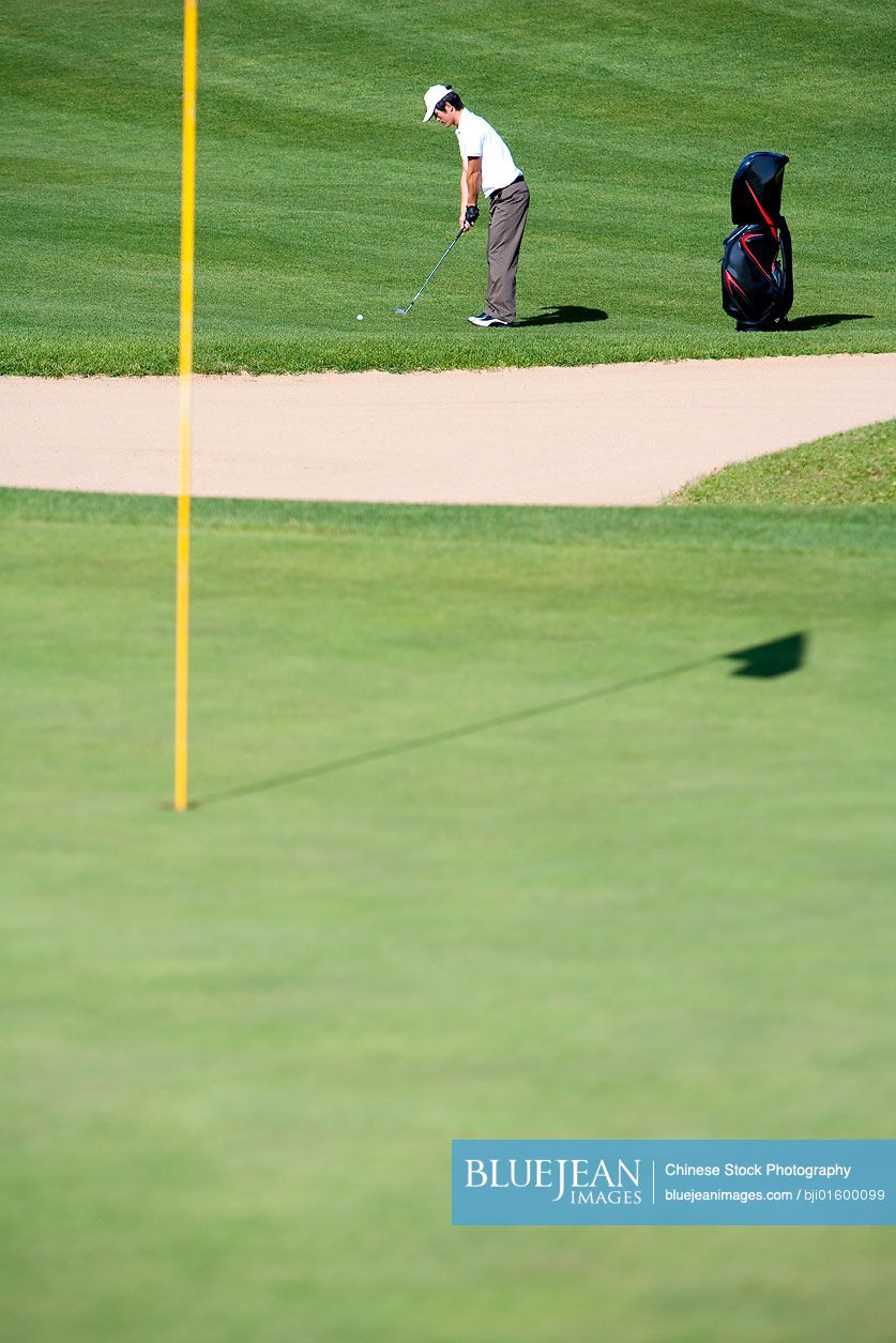 Young Chinese man preparing to take a golf swing