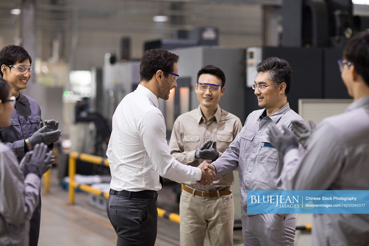 Businessman and engineer shaking hands in the factory