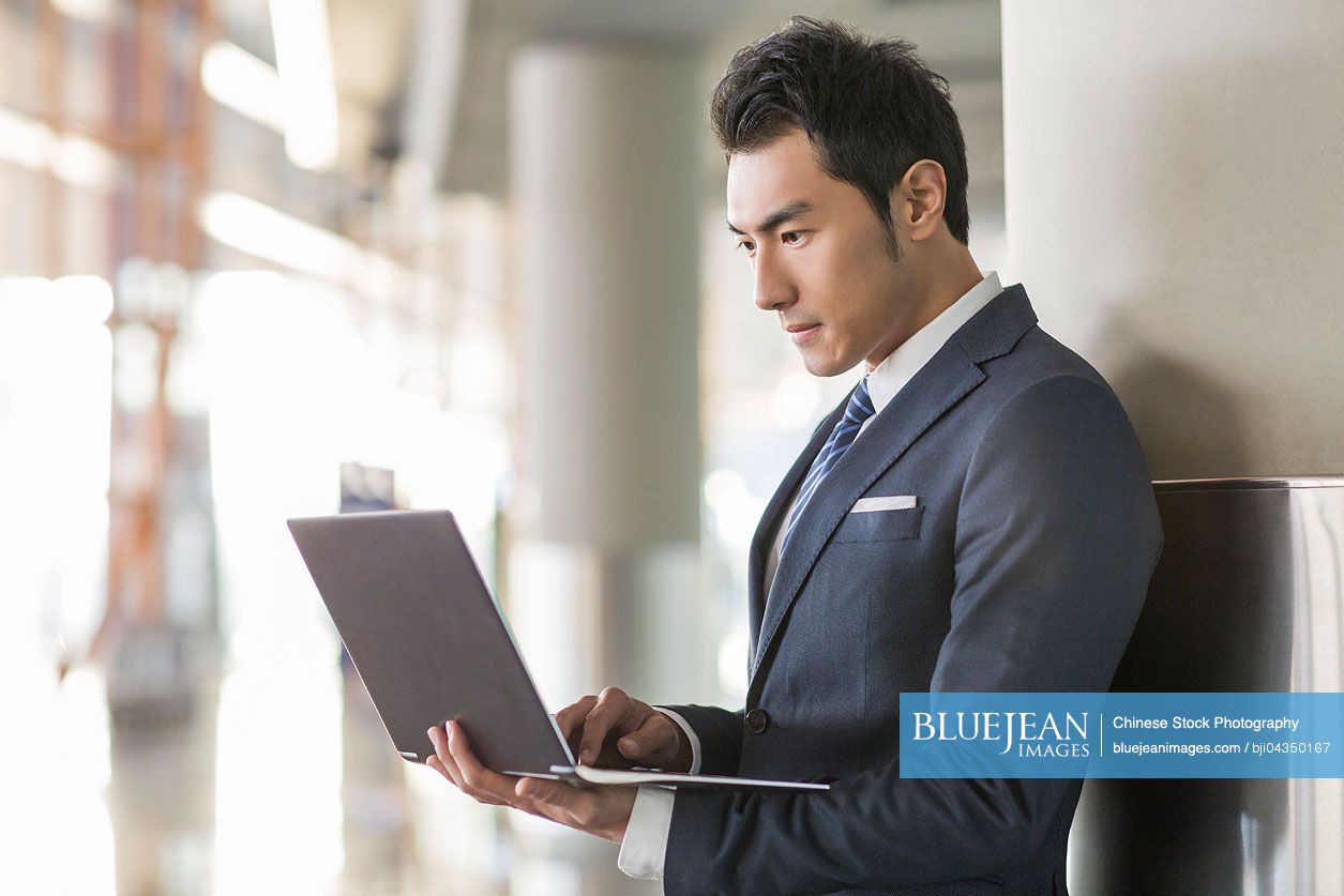 Young Chinese businessman using laptop in airport