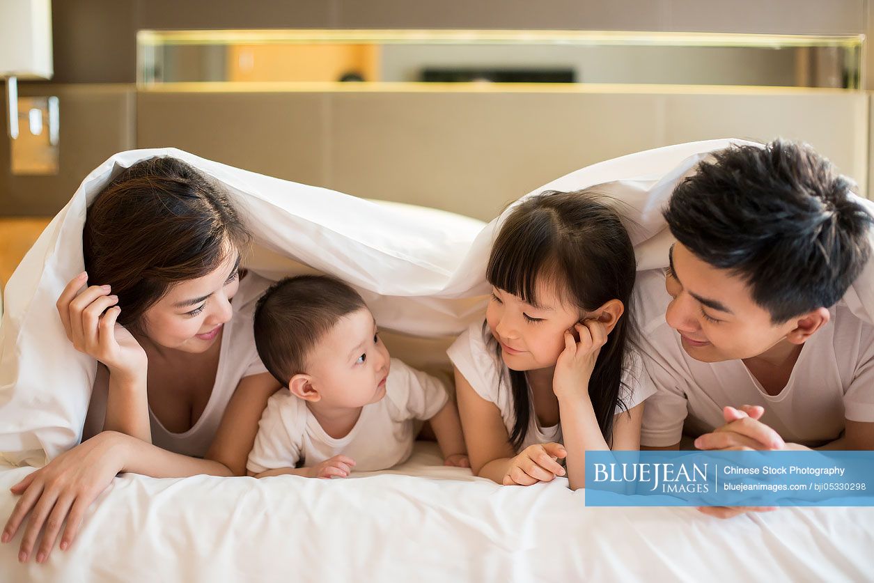 Happy young Chinese family lying on bed