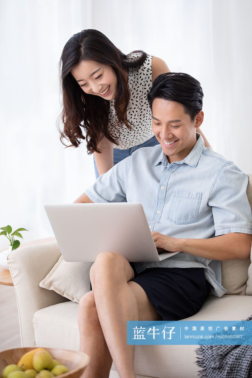 快乐的年轻情侣在客厅使用笔记本电脑-蓝牛仔影像-中国原创广告影像素材