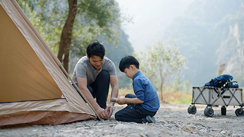 Little Chinese boy setting up camping tent together with his father