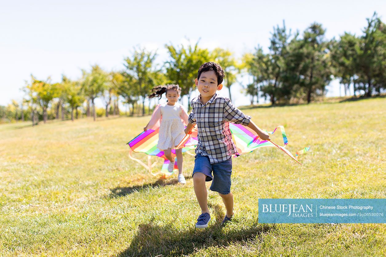 Happy Chinese children running with kites on meadow