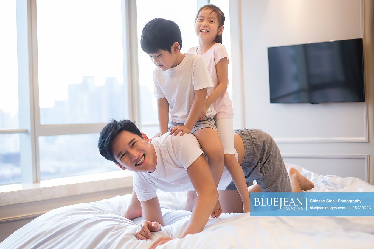 Cheerful young Chinese family having fun on a bed