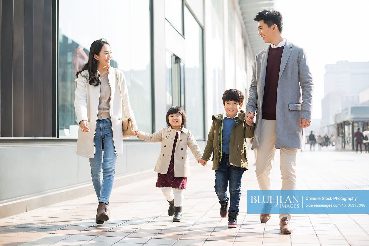 Cheerful young Chinese family holding hands walking