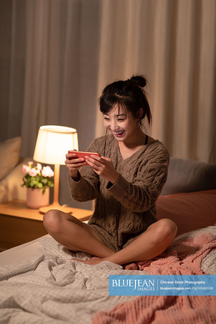 Young Chinese woman playing mobile games at home