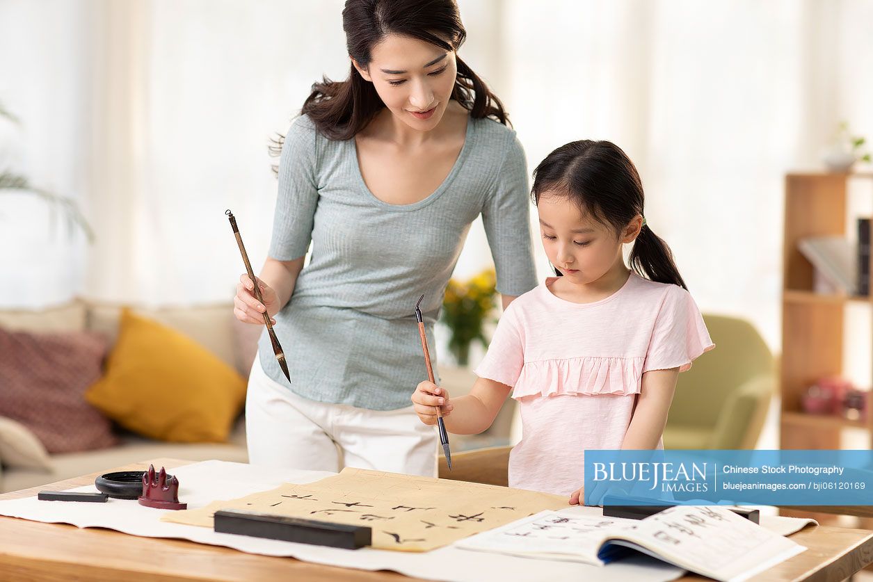 Happy Chinese mother and daughter writing calligraphy at home