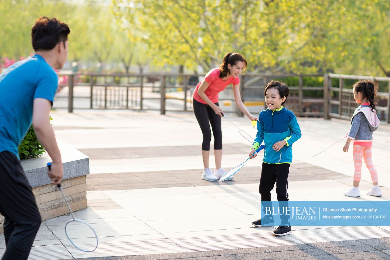 Happy young Chinese family playing badminton in park