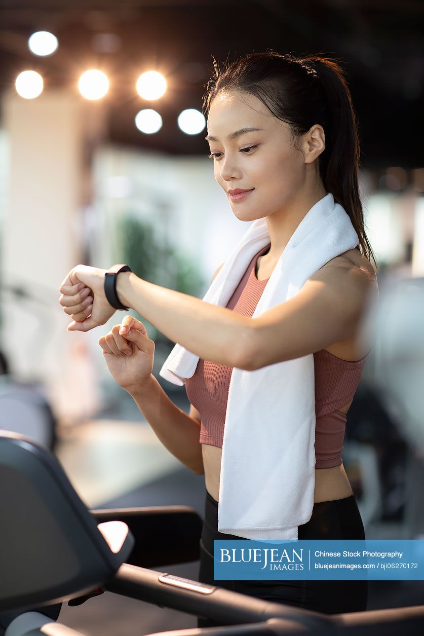 Young Chinese woman checking smart watch at gym
