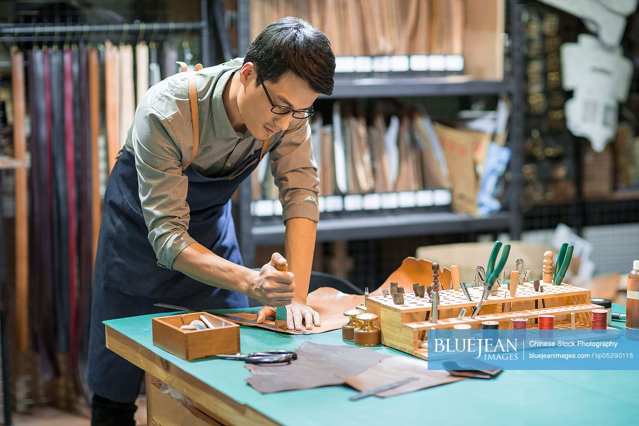 Young Chinese leather craftsman working in studio 