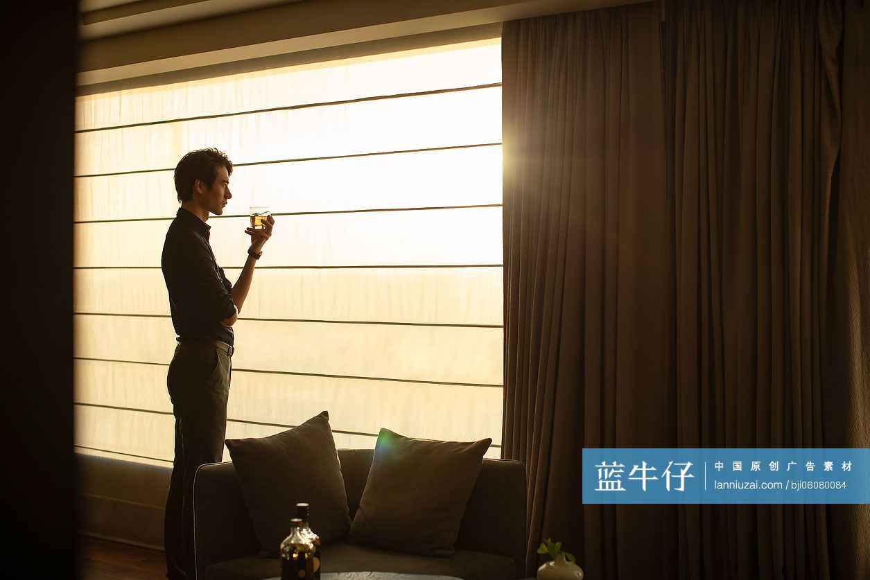 年轻商务男士站在窗前喝酒