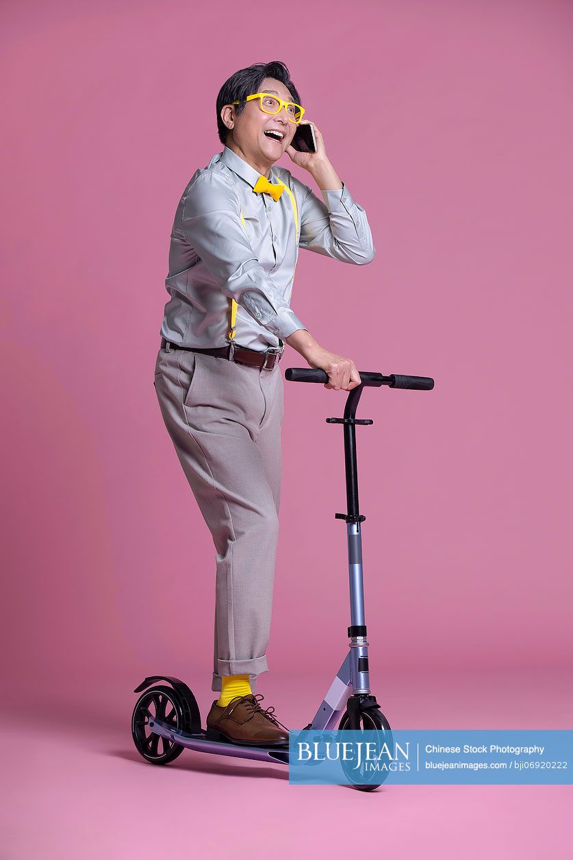 Cheerful senior Chinese man riding scooter