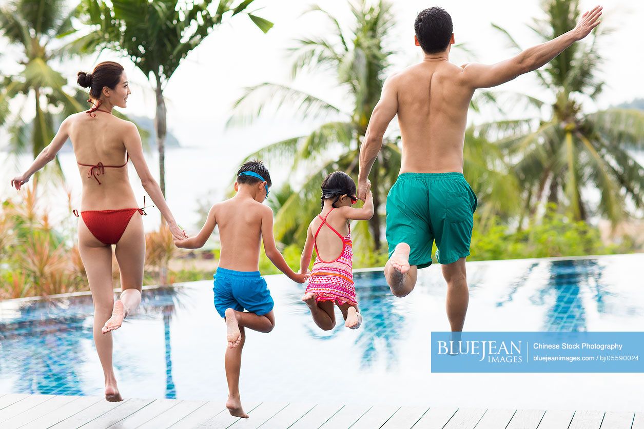 Happy young Chinese family jumping into swimming pool