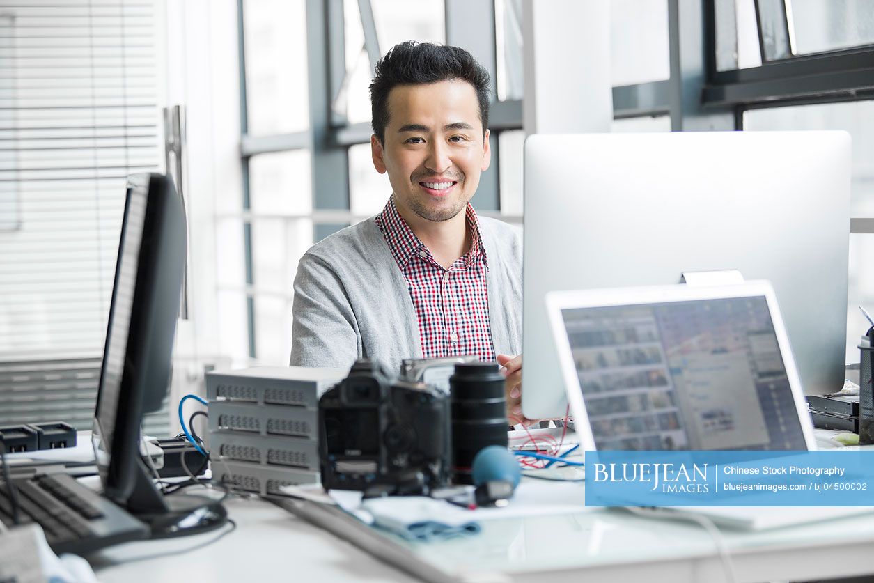 Male Chinese photographer working in office with computer