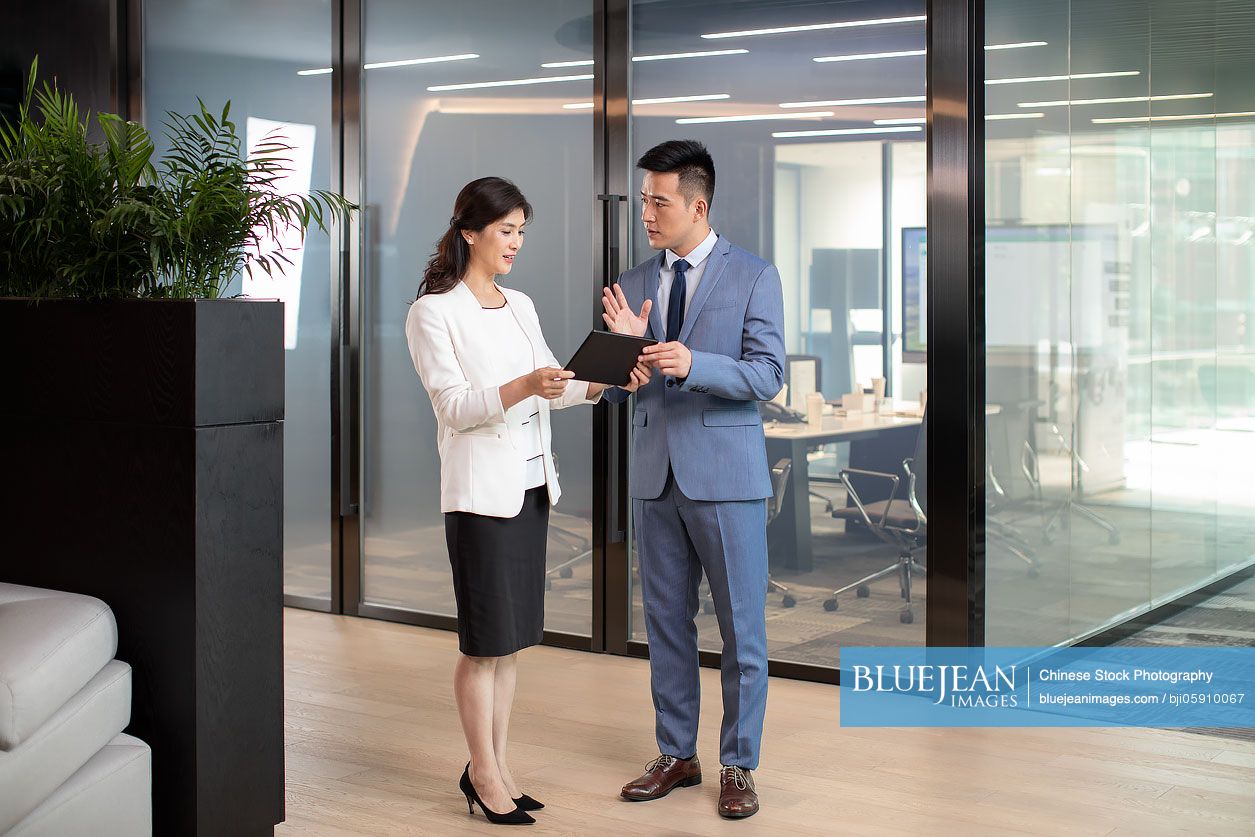Two successful Chinese business people talking in office hallway