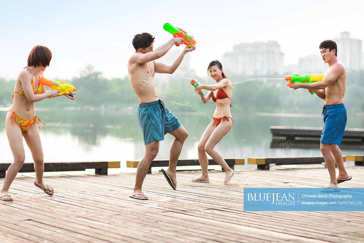 Happy young Chinese friends playing with squirt guns