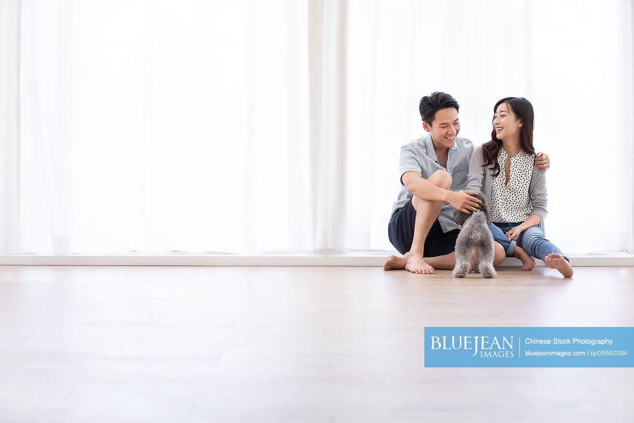 Happy young Chinese couple playing with dog in living room